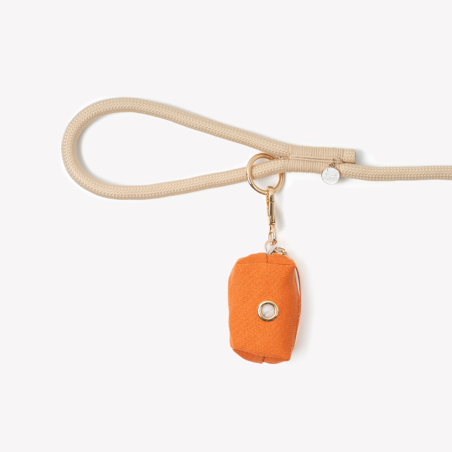 Beige dog leash with an orange bag attachment on a white background