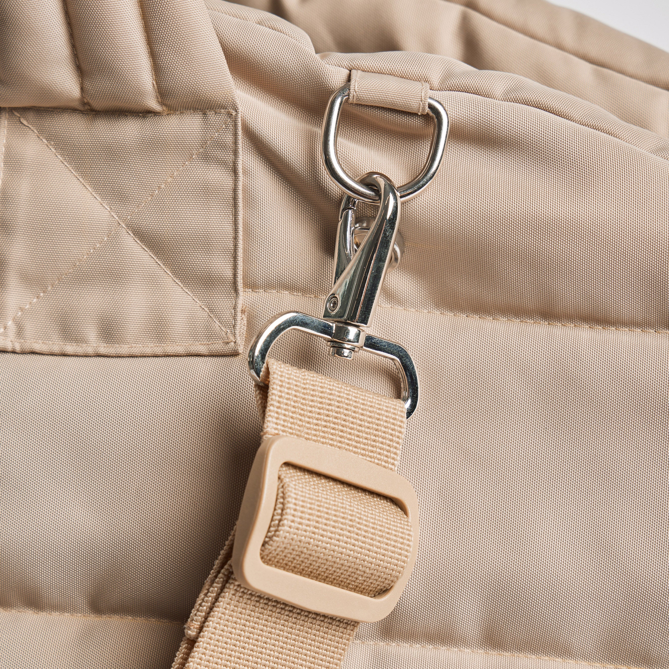 Close-up of a beige bag with a strap and metal clip on a light background