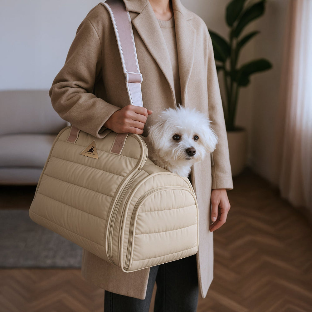 Person holding a beige pet carrier with a small white dog inside, wearing a beige coat.
