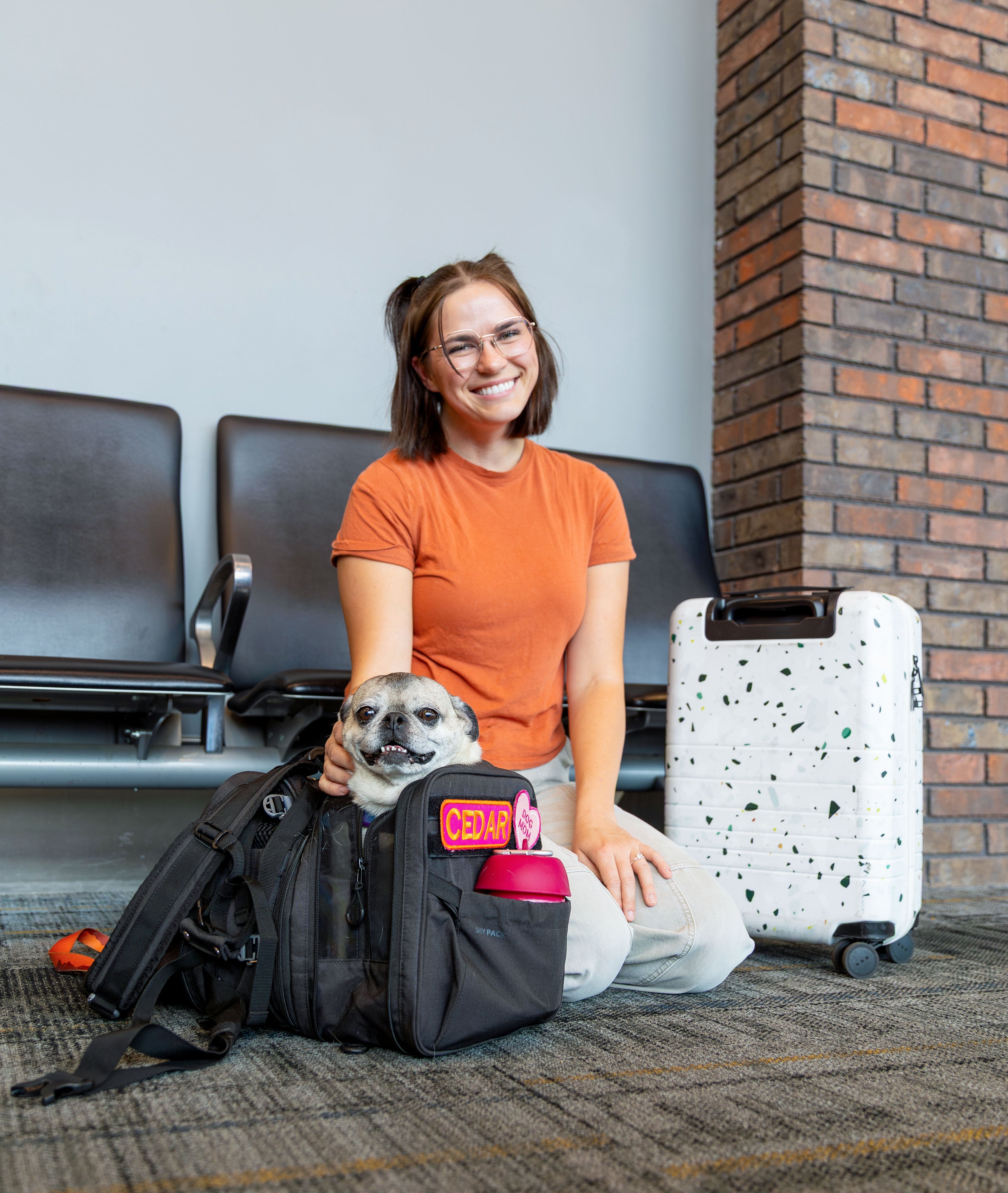 Woman with a dog in a pet carrier at an airport.