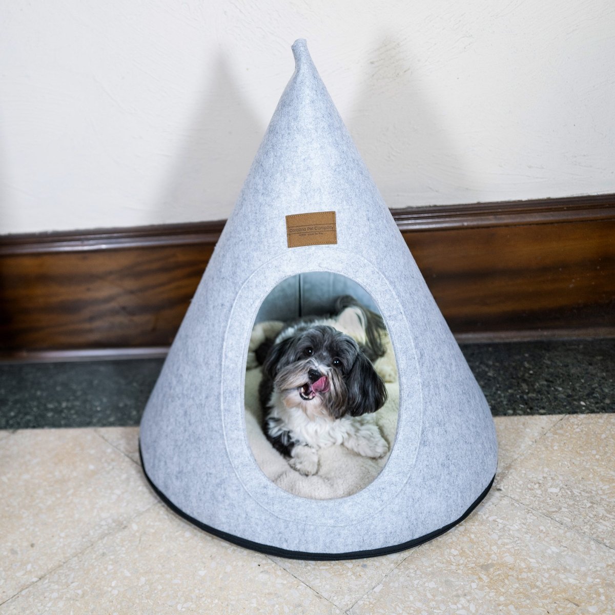 Gray pet cone-shaped cave bed with a small dog peeking out on a carpeted floor.