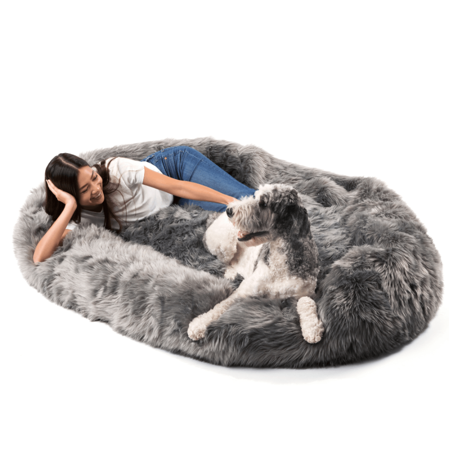 Woman lying on a large gray fluffy bed with a dog.