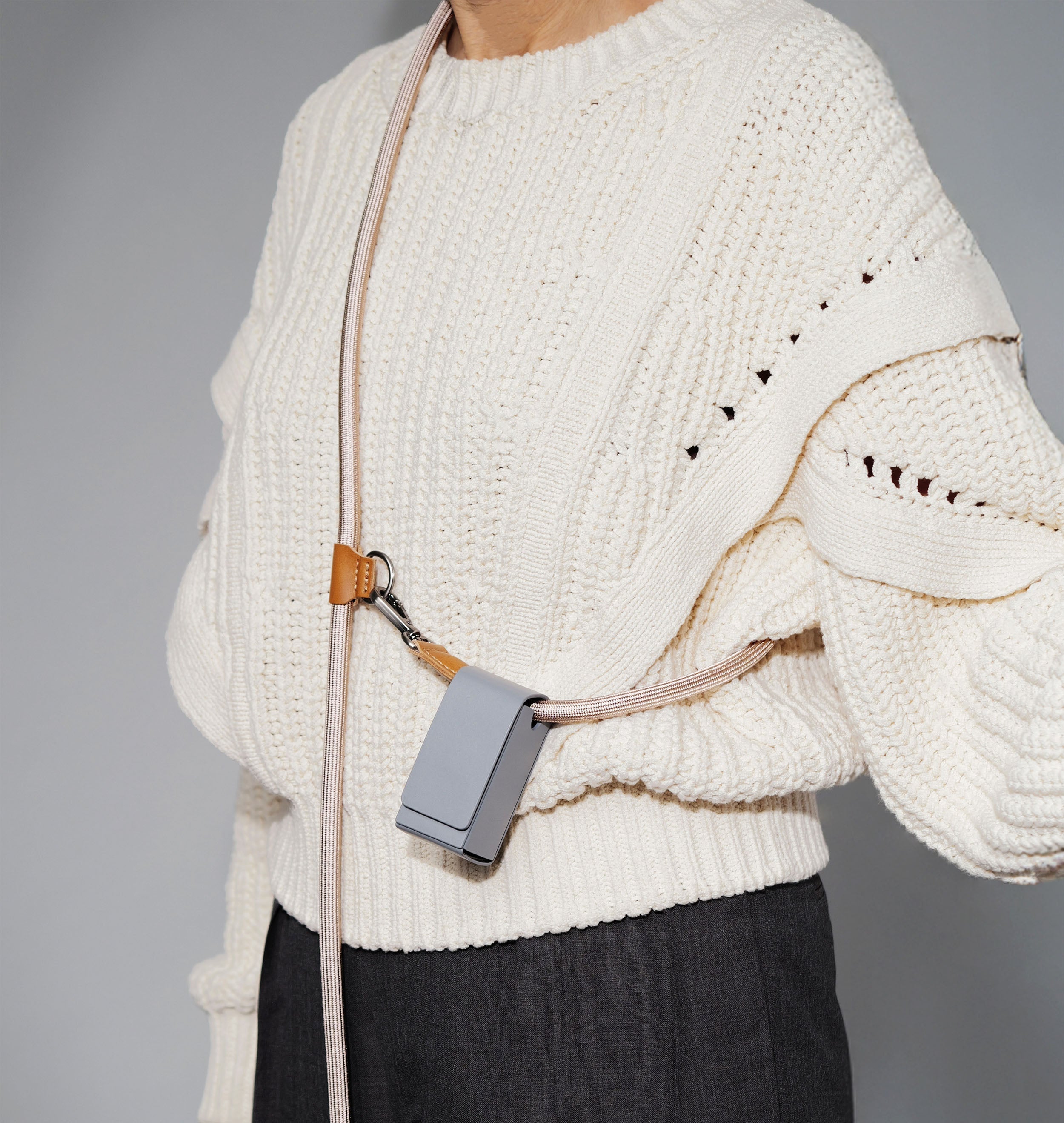 dog owner wearing a white sweater with a crossbody dog leash over their shoulder against a gray background, a hand-free dog leash
