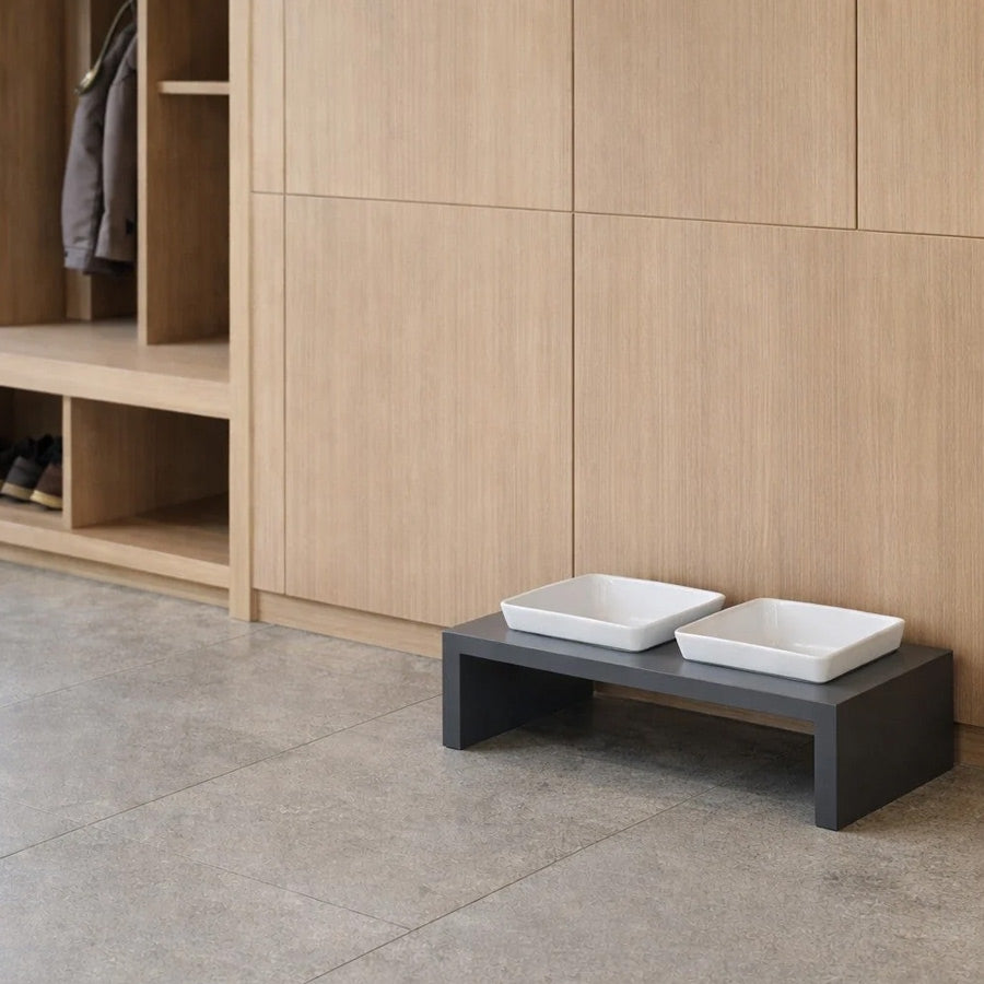 A modern elevated pet feeder with grey stand, holding two white square ceramic pet bowls by bowsers