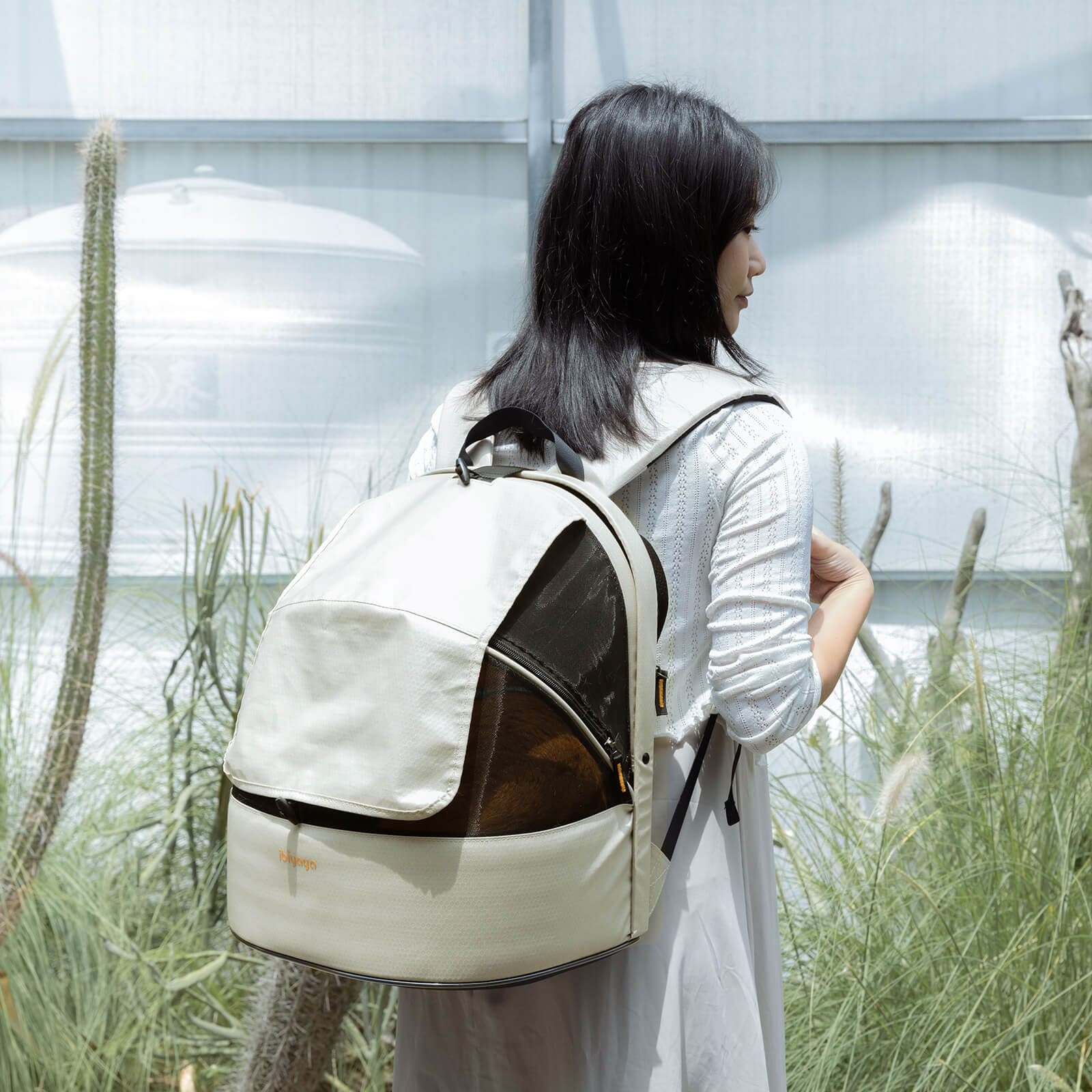 Woman carrying a large beige backpack small pet carrier for travel.