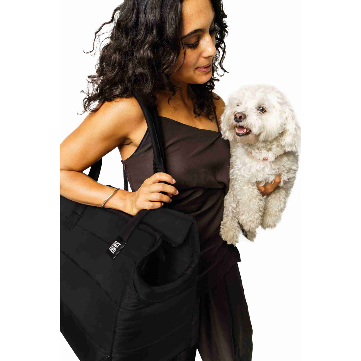 Woman holding a small white dog next to the large JUST FRED Subway Tote