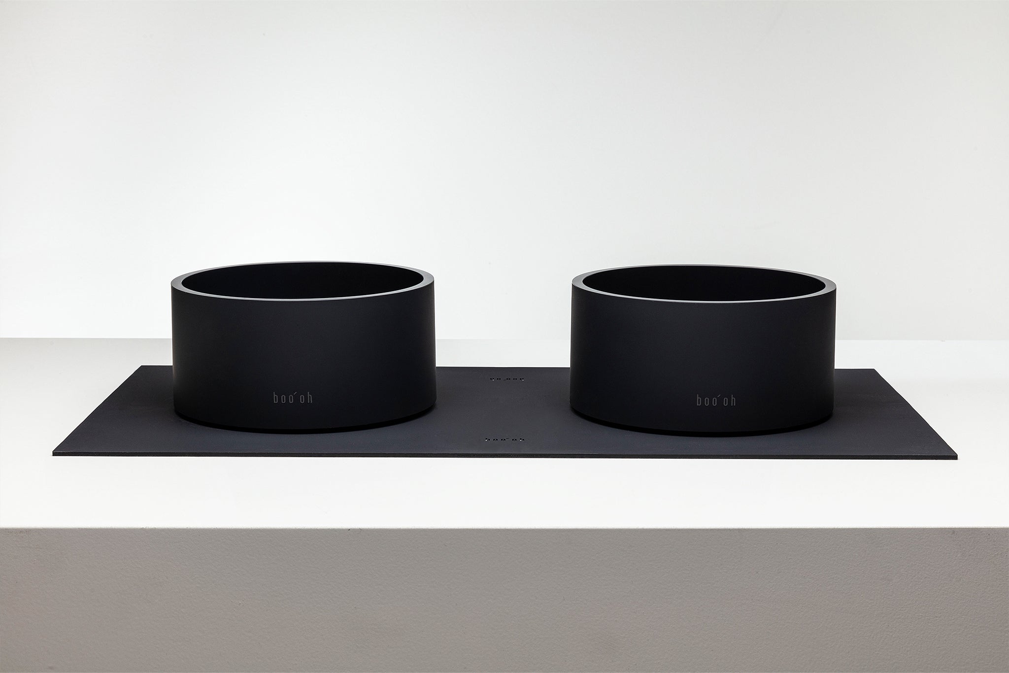 Two black pet bowls on a black mat with a white background