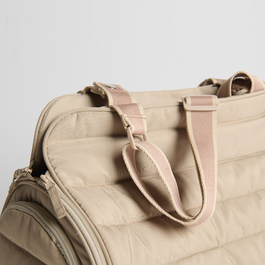 Beige quilted pet bag carrier with pink straps on a light gray background