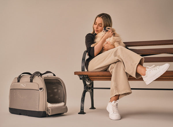 Woman sitting on a bench with a dog in her arms, next to a Tavo small dog pet carrier.