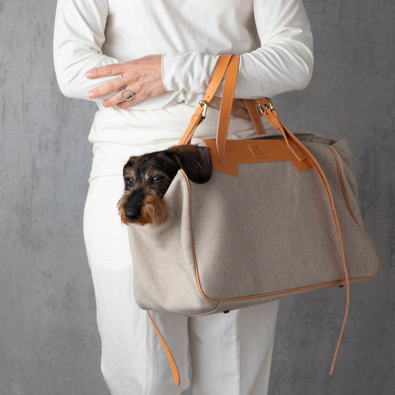 Dog lover holding a luxury dog carrier with leather handles and organic cotton.